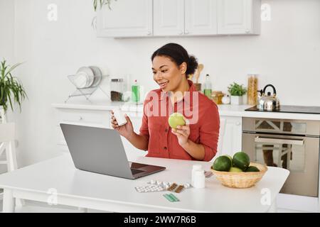 nutritionniste afro-américain tenant pomme et suppléments tout en offrant des conseils de santé en ligne Banque D'Images