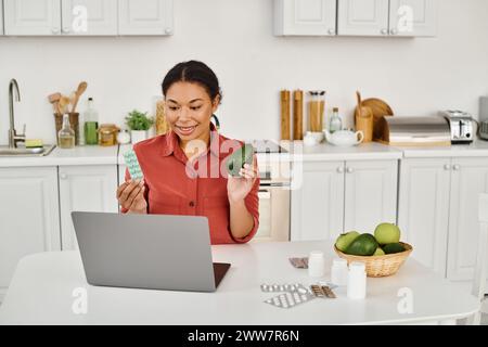 nutritionniste afro-américain tenant avocat et suppléments tout en donnant des conseils de régime à partir d'un ordinateur portable Banque D'Images