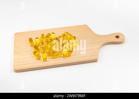 Gélules d'oméga 3 dispersées sur le dessus d'une planche à découper isolée sur fond blanc. Banque D'Images