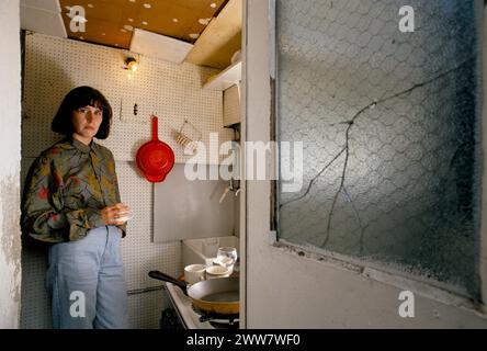 Mauvais logement des années 1990 mauvais logement loué par des particuliers de mauvaise qualité. Jeune femme adulte locataire dans la cuisine de son appartement. Vitre de la porte d'entrée avant fissurée, cassée. Londres Angleterre Royaume-Uni. Vers 1995 HOMER SYKES Banque D'Images