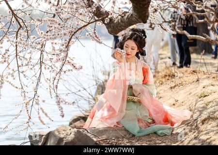 Pékin, Chine. 22 mars 2024. Une jeune fille portant le Hanfu, un style de vêtements traditionnellement porté par le peuple han, pose pour une photo avec des fleurs de pêche au Palais d'été de Pékin, capitale de la Chine, le 22 mars 2024. Récemment, les fleurs de printemps telles que les fleurs de pêche sont en pleine floraison au Palais d'été de Pékin, attirant un grand nombre de touristes. Crédit : Chen Yehua/Xinhua/Alamy Live News Banque D'Images