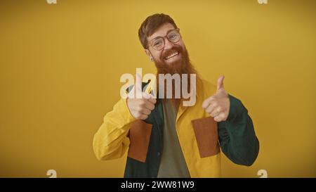 Un homme roux joyeux avec une barbe donnant les pouces devant un fond jaune. Banque D'Images