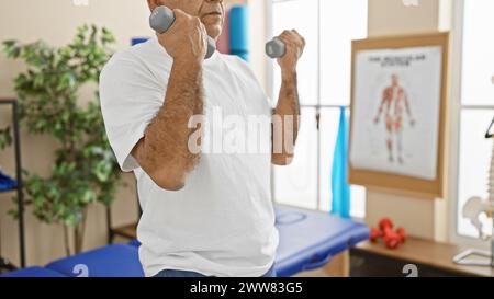 Un homme hispanique mature exerçant avec des haltères dans une clinique de physiothérapie, suggérant la santé et la récupération. Banque D'Images