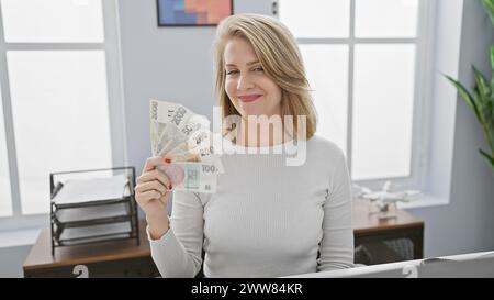 Femme blonde au bureau tenant la monnaie tchèque avec une expression joyeuse Banque D'Images