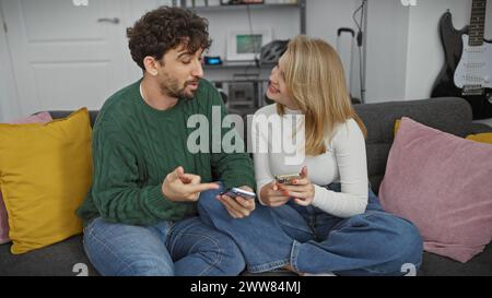 Un couple s'engage dans une conversation joyeuse sur un canapé avec des oreillers colorés dans un salon moderne. Banque D'Images