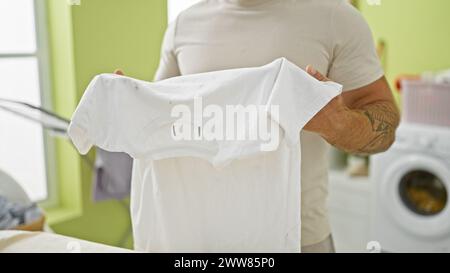 Jeune homme barbu pliant le linge dans une buanderie lumineuse. Banque D'Images