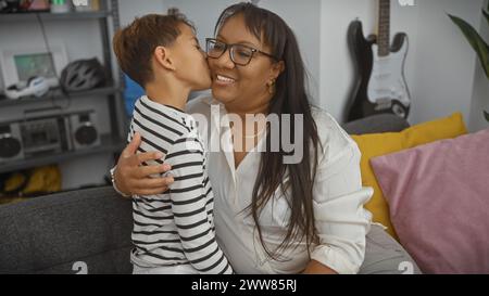 Une femme aimante et son jeune fils partagent un moment tendre, embrassant sur la joue, dans un cadre de salon confortable. Banque D'Images