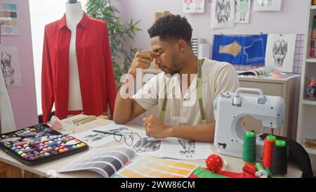 Homme afro-américain concentré dans un atelier coloré, entouré de dessins, de tissus et d'une machine à coudre. Banque D'Images