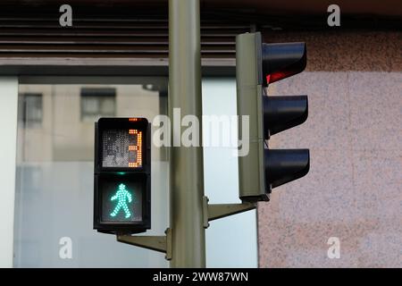 Feu de circulation piéton avec signal permissif vert et compte à rebours, petit homme vert marchant, numéro 3, fond de bâtiment. Les feux de circulation régulent le mouvement des piétons sur la chaussée Banque D'Images