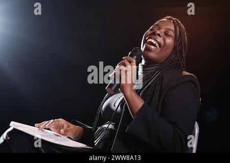 Portrait de femme noire riant sur scène et tenant le microphone tout en jouant dans l'espace de copie de spectacle de comédie Banque D'Images