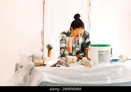 Une jeune femme attrayante se tient parmi les matériaux de construction et l'inventaire. Une charmante fille en vêtements décontractés pense à faire des réparations de maison. Banque D'Images