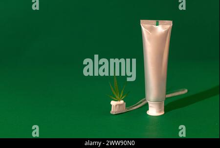 Une brosse à dents en plastique transparent avec dentifrice blanc cannabis CBD avec feuille de cannabis. Arrière-plan isolé vert. Soins de santé et hygiène dentaire conc Banque D'Images