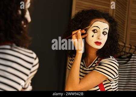 Jeune femme appliquant le maquillage mime près du miroir à l'intérieur Banque D'Images