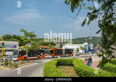 Cartagena, Colombie - 25 juillet 2023 : Transports publics, 2 sortes de bus publics orange dans une rue animée sous un paysage nuageux bleu et un paysage de feuillage vert Banque D'Images