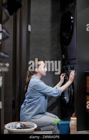 Femme allumez la machine à laver automatique ou sélectionnez le programme avec le bouton sur le panneau de commande dans la salle de bain, les appareils modernes à la maison. Banque D'Images