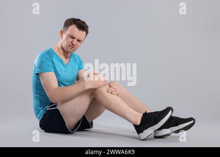 Homme souffrant de douleurs aux jambes sur fond gris Banque D'Images