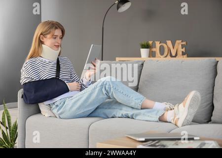 Jeune femme blessée après un accident en utilisant un ordinateur tablette sur le canapé à la maison Banque D'Images