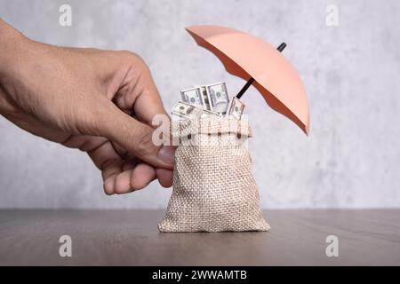 Main tenant un parapluie protégeant un sac d'argent. Sécurité financière, concept d'assurance protection du revenu. Banque D'Images