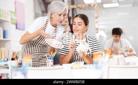 Céramiste expérimentée enseignant à la jeune fille à peindre la céramique dans un atelier de poterie Banque D'Images