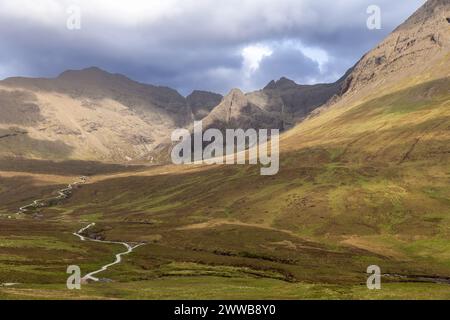 Un sentier touristique sinueux traverse la vallée verdoyante de l'île de Skye, conduisant les aventuriers vers les Fairy Pools sous un ciel spectaculaire Banque D'Images