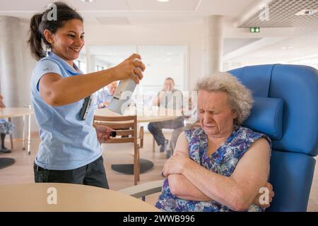 EHPAD - soignant malentendant pulvérisant de l'eau sur le visage d'un résident âgé pendant la forte chaleur estivale. Banque D'Images