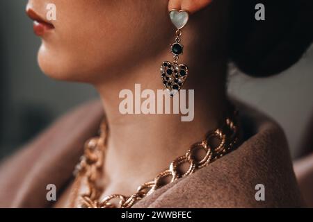 Une chaîne en or accrochée au cou d'une femme et une boucle d'oreille en forme de coeur. Beaux accessoires de bijoux de luxe élégants Banque D'Images