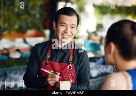 Serveur vietnamien joyeux parlant au client du restaurant Banque D'Images