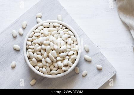 Haricots blancs séchés non cuits dans un bol ou une cuillère sur la table. Tas de légumineuses haricots de fond ( Phaseolus vulgaris ) Banque D'Images