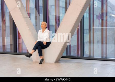 Femme d'affaires senior assise au milieu de la colonne architecturale Banque D'Images