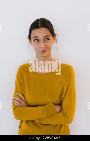 Jeune femme d'affaires debout avec les bras croisés et faisant face devant le mur blanc Banque D'Images