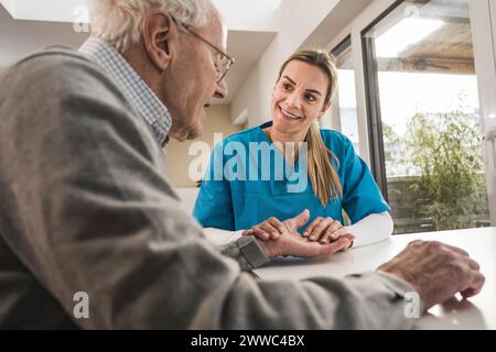 Soignant souriant à domicile prenant le pouls de l'homme Banque D'Images