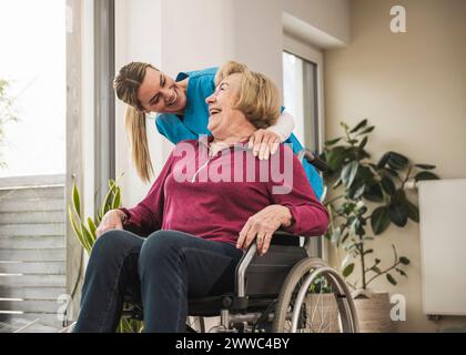 Soignant heureux à domicile avec une femme âgée assise en fauteuil roulant Banque D'Images