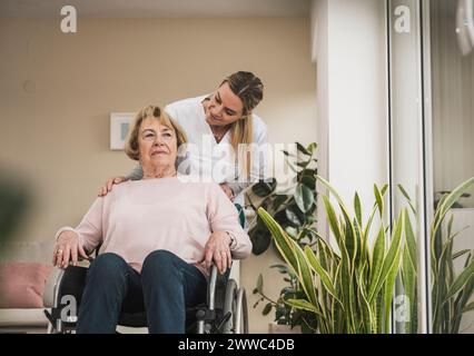 Soignant à domicile avec une femme âgée assise en fauteuil roulant à la maison Banque D'Images