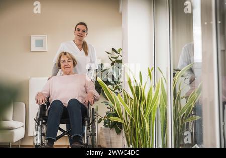 Soignant souriant à domicile avec une femme assise en fauteuil roulant Banque D'Images
