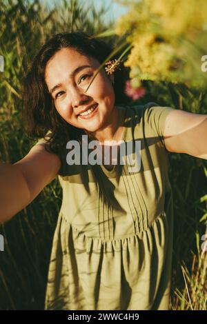 Femme mature souriante prenant selfie au milieu de l'herbe dans le champ Banque D'Images