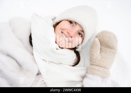 Femme souriante couchée sur la neige dans des vêtements chauds Banque D'Images