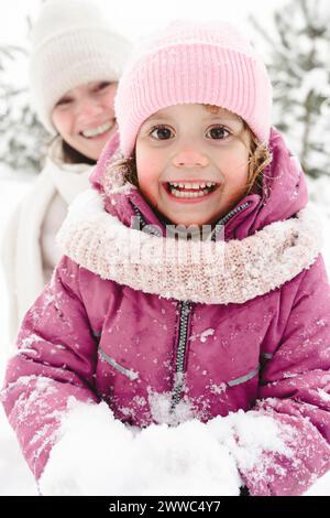 Fille excitée tenant la neige avec mère en arrière-plan au parc d'hiver Banque D'Images