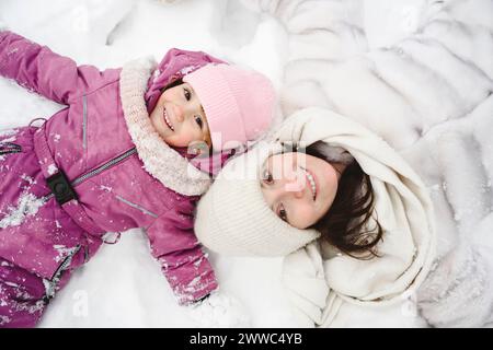 Fille heureuse allongée sur la neige avec mère Banque D'Images