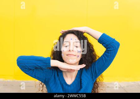 Femme avec des autocollants sur le visage assis devant le mur jaune Banque D'Images