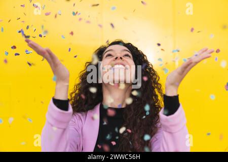 Femme joyeuse jouant avec des confettis sur fond jaune Banque D'Images