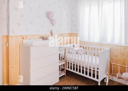 Chambre d'enfant décorée avec lit bébé et commode près de la fenêtre Banque D'Images