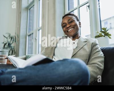 Heureuse femme d'affaires portant blazer assis sur le canapé au bureau Banque D'Images