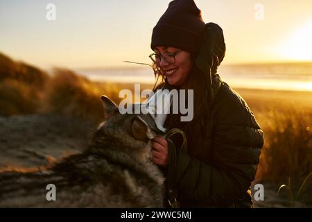 Femme souriante caressant chien Husky à la plage Banque D'Images