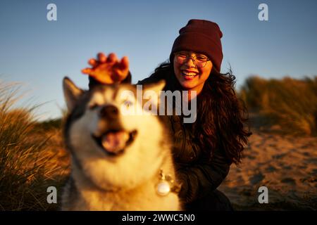 Jeune femme joyeuse s'amusant avec le chien au coucher du soleil Banque D'Images