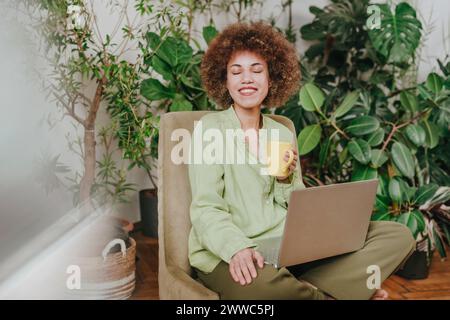 Freelance souriante assise les yeux fermés et ordinateur portable à la maison Banque D'Images