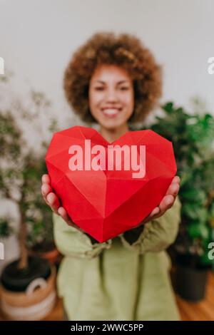 Femme souriante tenant le coeur de papier rouge près des plantes Banque D'Images
