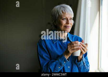 Femme mature souriante tenant une tasse à café à la maison Banque D'Images