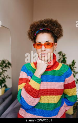 Jeune femme portant des lunettes de soleil et debout avec la main sur le menton à la maison Banque D'Images