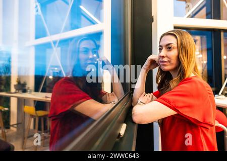 Femme d'affaires réfléchie regardant par la fenêtre dans le bureau Banque D'Images