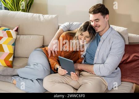 Aimer jeune couple en utilisant tablette PC sur canapé Banque D'Images